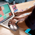 Person using a laptop with a design software on screen, surrounded by color swatches and a tablet.