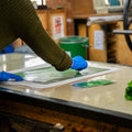 Person wearing gloves working on a project with green materials in a workshop setting