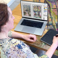 Person sitting at a table with a laptop displaying art software and digital drawing pad.