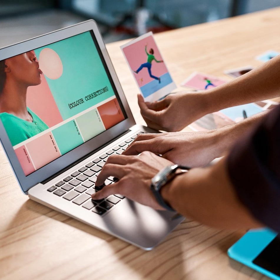 Person using a laptop with a design software on screen, surrounded by color swatches and a tablet.