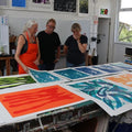 Group of people looking at large scale colorful prints on a table in a workshop setting.