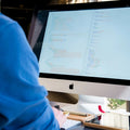 Person wearing a blue shirt using a computer with code on the screen