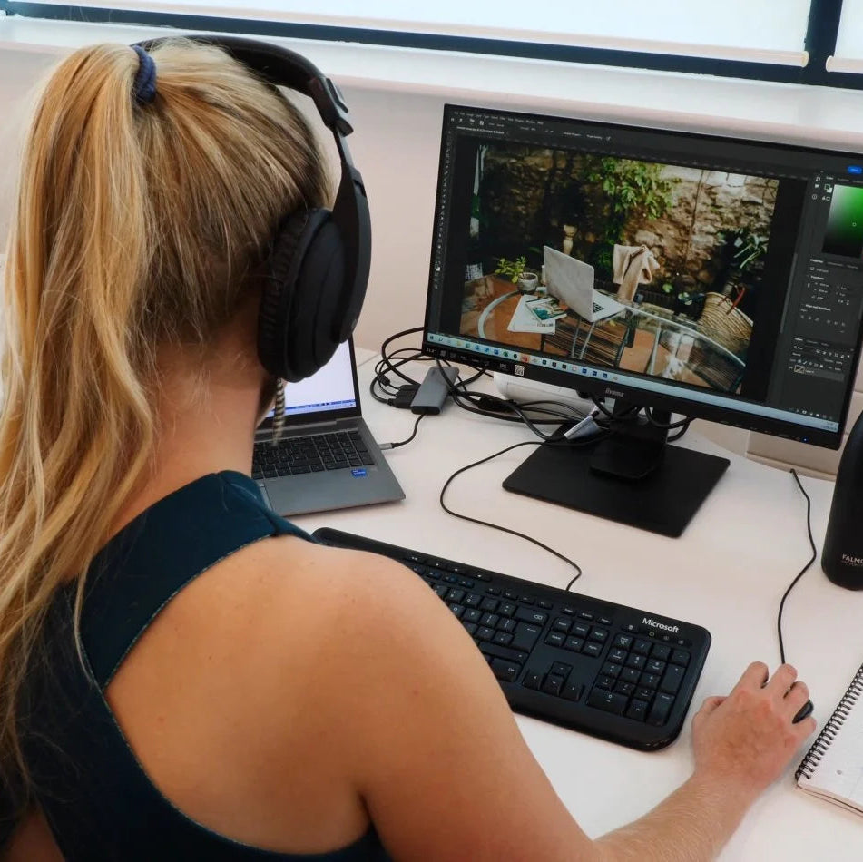 Person wearing headphones working on a computer with dual monitors at a desk.