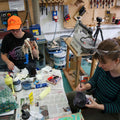 Two people working in a workshop with tools and materials on a table.