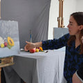 Two people in a studio setting, one pointing at a painting on an easel.